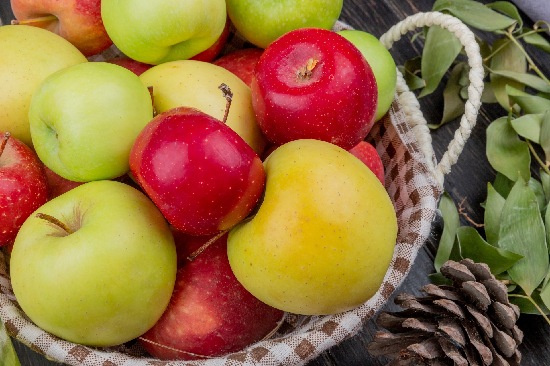 side-view-apples-basket-with-pinecone-leaves-wooden-surface